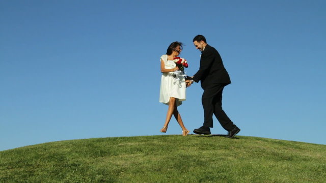 Bride and groom run over grassy hill