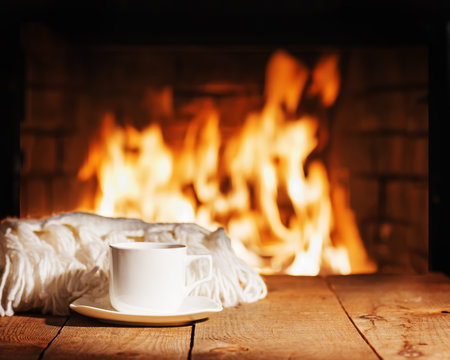 White cup of tea or coffee and woolen scarf near fireplace.