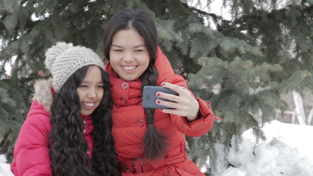 Smiling two girl taking a selfie with smartphone outdoors in warm clothes