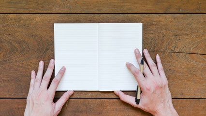 Man hands with pen and empty notepad on wooden table.