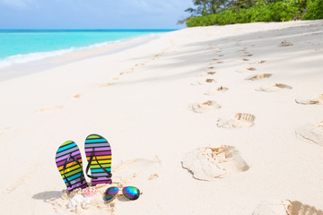 Multicolored flip-flops and sunglasses on a sunny beach..Tropica
