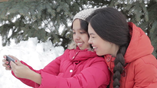 Smiling two girl taking a selfie with smartphone outdoors in warm clothes