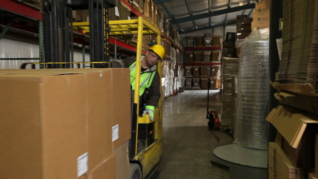 Forklift operator in a shipping warehouse moves pallets of inventory
