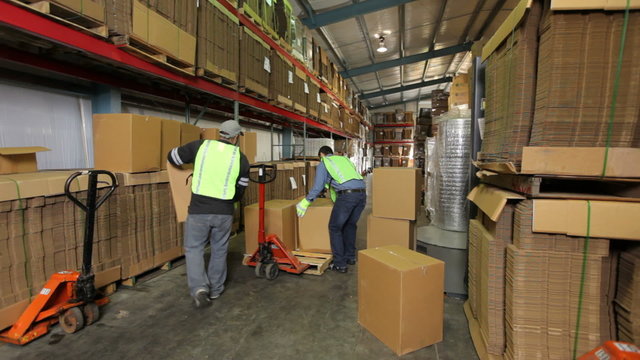 Two workers in shipping warehouse stacking boxes