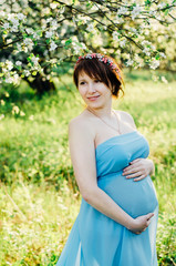 Fototapeta na wymiar Smiling pregnant woman in blooming garden touching her belly 