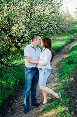 Naklejka na ściany i meble Happy pregnant couple kissing in booming garden 