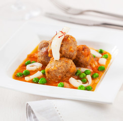 Meatballs with squid and green peas in sauce.