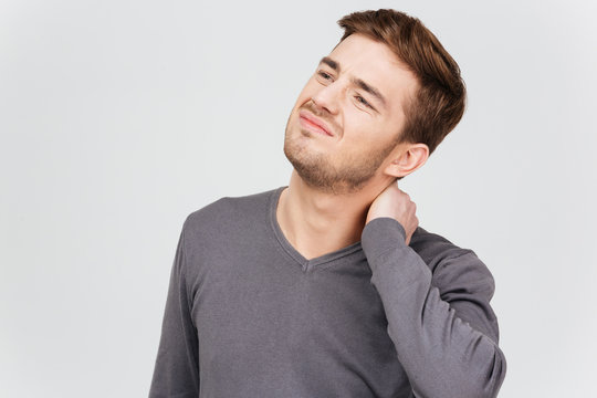 Sad unhappy man in grey pullover suffering from neck pain