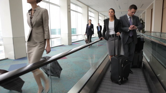 Business people at airport travel along moving walkway