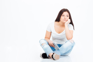 Pensive casual woman sitting on the floor with tablet computer