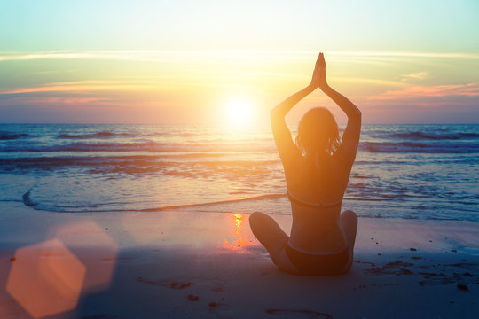 Silhouette of woman practicing yoga on the Sea beach.