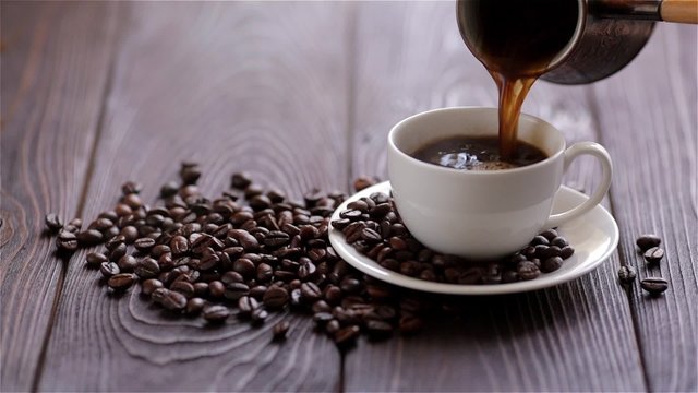 Pouring coffee from a turks on wooden background with coffee beans