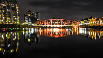 Fototapeta premium Reflections on a stale tranquil water at night from a highlighted industrial bridge in Salford, Manchester, United Kingdom