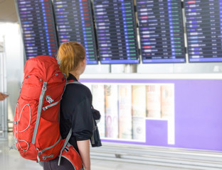 Young woman with backpack in airport near flight timetable