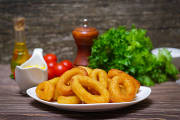 deep fried calamari with sauce and salad on a wooden background