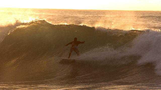 Surfer rides wave at sunset, slow motion