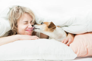 Blonde beautiful Woman and dog playfully indulge in fun on the bed. Dog bites the girl's nose....