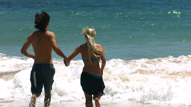 Young couple running into ocean, slow motion