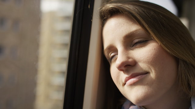 Attractive young woman closes her eyes whilst relaxing on a train, in slow motion