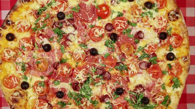 Rotating pizza with cheese, tomatoes and olives on the red tablecloth close-up

