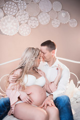 Husband hugging his pregnant wife in white lingerie on a light background, lifestyle, waiting, belly