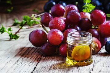 Healing grape seed oil in a glass jar, fresh pink grapes on old