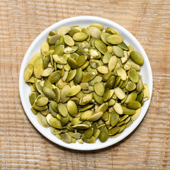 Pumpkin seeds in the plate, on wooden background