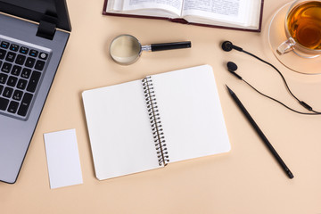 Office table desk with supplies, white blank note pad, cup, pen, pc, crumpled paper, flower on wooden background. Top view