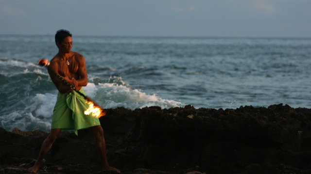 Hawaiian fire knife dancer performs by ocean, slow motion