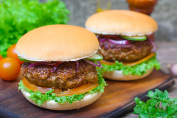 Juicy burgers hamburger with a big beef cutlet, tomato, lettuce and onion on wooden background