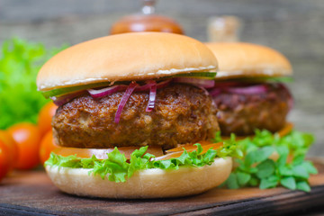 Juicy burgers hamburger with a big beef cutlet, tomato, lettuce and onion on wooden background