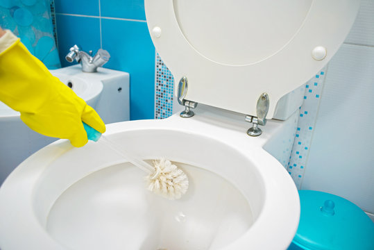 A woman cleans a bathroom toilet with a scrub brush.