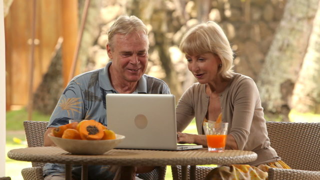 Senior couple at tropical resort use laptop computer
