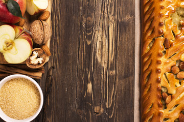 Apple pie with almonds and cinnamon and ingredients over brown wooden table. Space for text