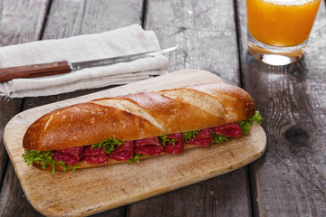 baguette sandwich with salami and herbs on a wooden surface