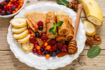 Breakfast. Pancakes with honey and fresh berries - raspberries, cranberries, sea buckthorn and  cowberry. Selective focus
