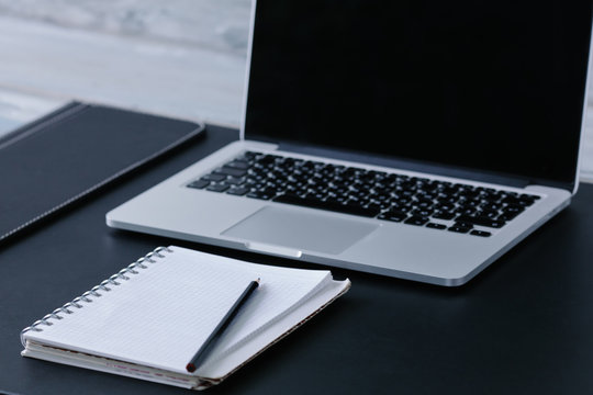 clean white sheet of notebook with the pencil near the laptop on the black leather desktop on a wooden table vintage