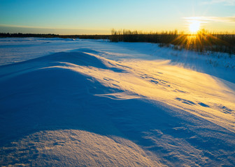 Winter landscape with the setting sun in  snowy field.