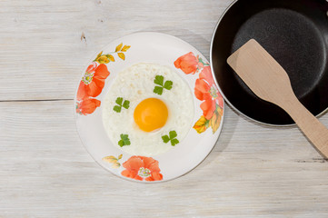 Fried eggs in a plate with a frying pan on a wooden background