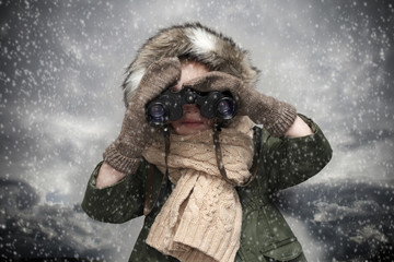 Child is looking through the binoculars at snowy and cloudy background