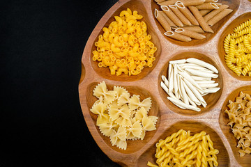 Various mix of pasta on wooden bowl and black background.