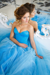 Fototapeta na wymiar Beautiful bride in gorgeous blue dress Cinderella style in a morning sitting near mirror