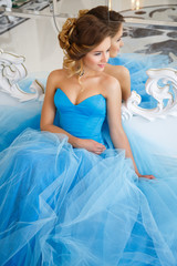 Fototapeta na wymiar Beautiful bride in gorgeous blue dress Cinderella style in a morning sitting near mirror