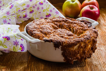 Apple pie in a white baking dish on the wooden background.