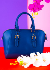 blue fashionable female bag with flowers orchid on a bright background