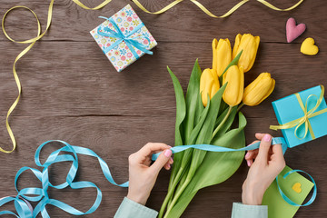 Female hands with tulips and gift box on wood 
