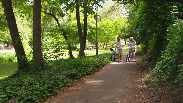 Mature couple walking bicycles and talking