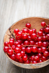 Redcurrant on a branch close to a wooden bowl.