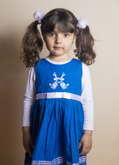 Small Caucasian girl putting her hand on her cheek Posing with blue dress standing inside studio