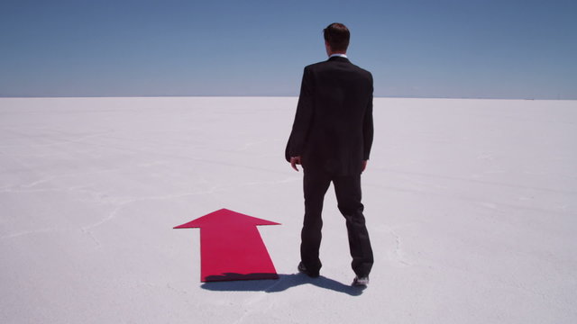 Businessman walks by red arrow at salt flat